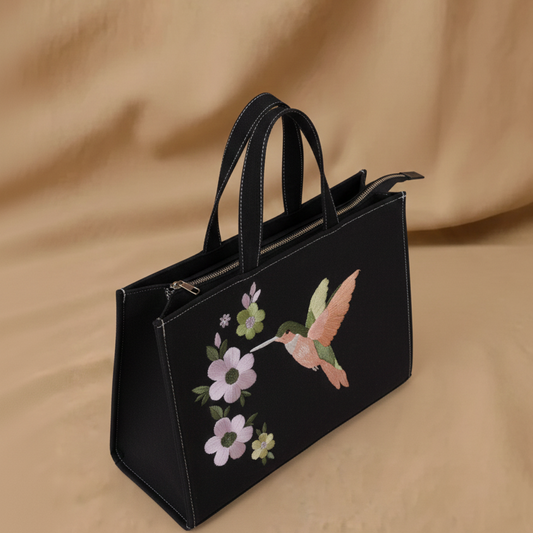 Black handbag with floral and hummingbird embroidery on a beige background