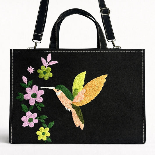 Black handbag with colorful hummingbird and floral embroidery on a white background