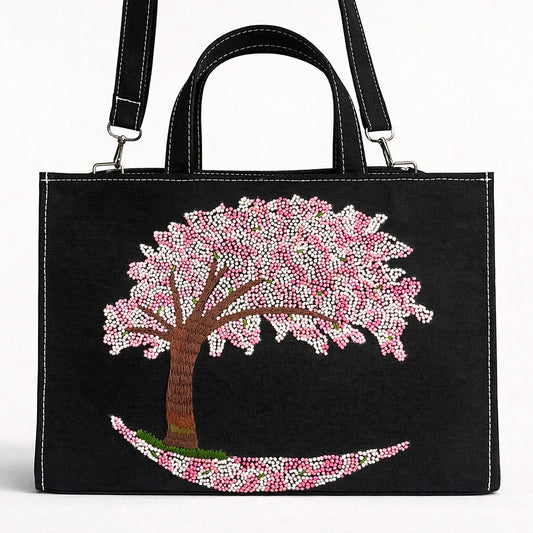 Black handbag with a pink floral tree design on a white background
