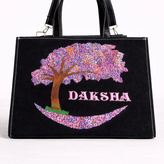 Black handbag with a decorative tree design and 'Daksha' text on a white background