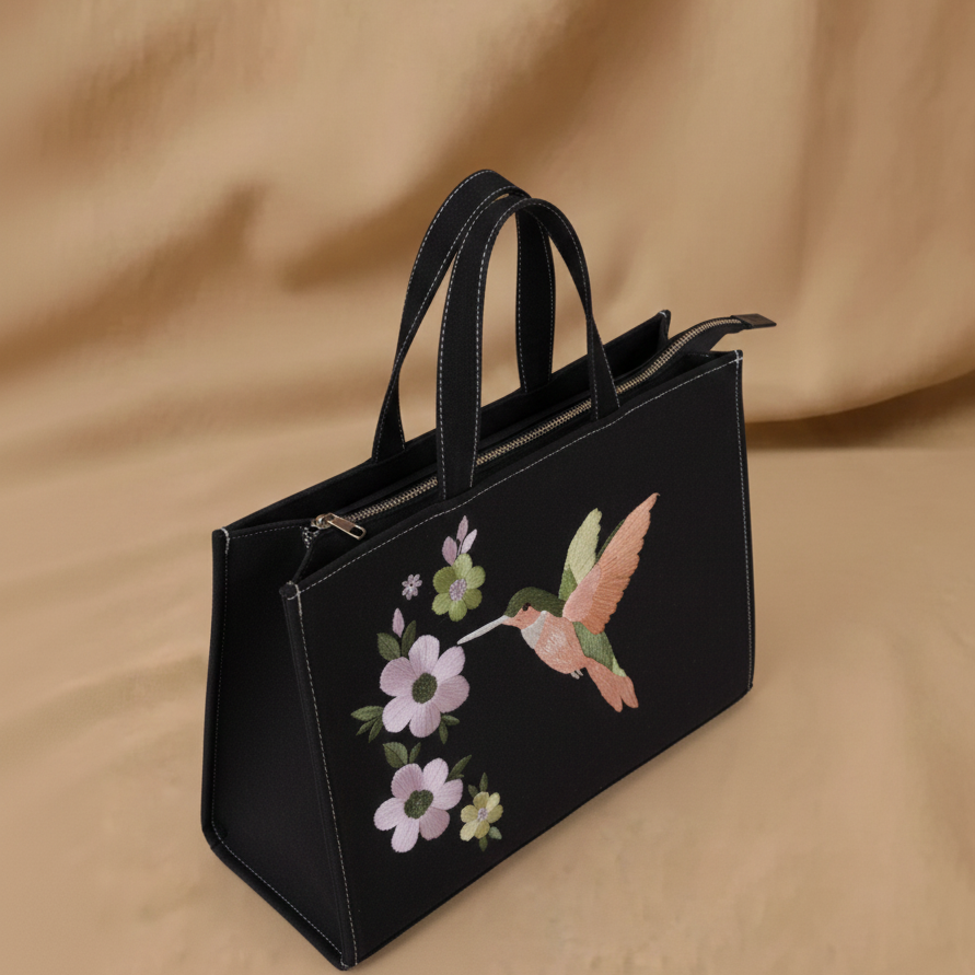 Black handbag with floral and hummingbird embroidery on a beige background
