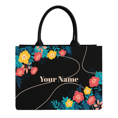 Black tote bag with colorful floral design and space for personalization on a white background