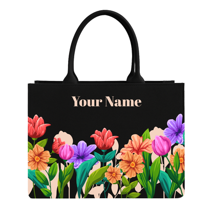 Black tote bag with colorful floral design and space for personalization on a white background