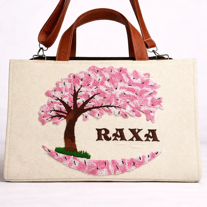 Handbag with cherry blossom design and 'RAXA' branding on a white background